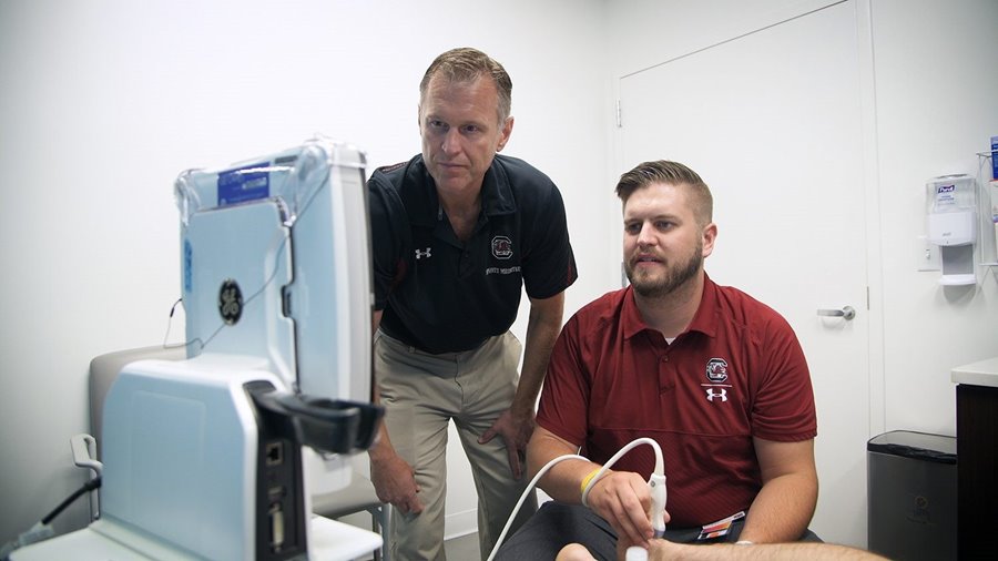 Sports medicine doctor working with trainee on ultrasound machine.